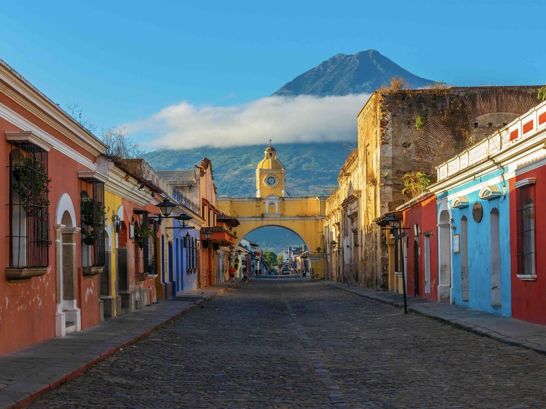 View of the main street and yellow Santa Catalina arch in Antigua with the Agua volcano during the Guatemala & Belize group tour with Other Way Round Travel