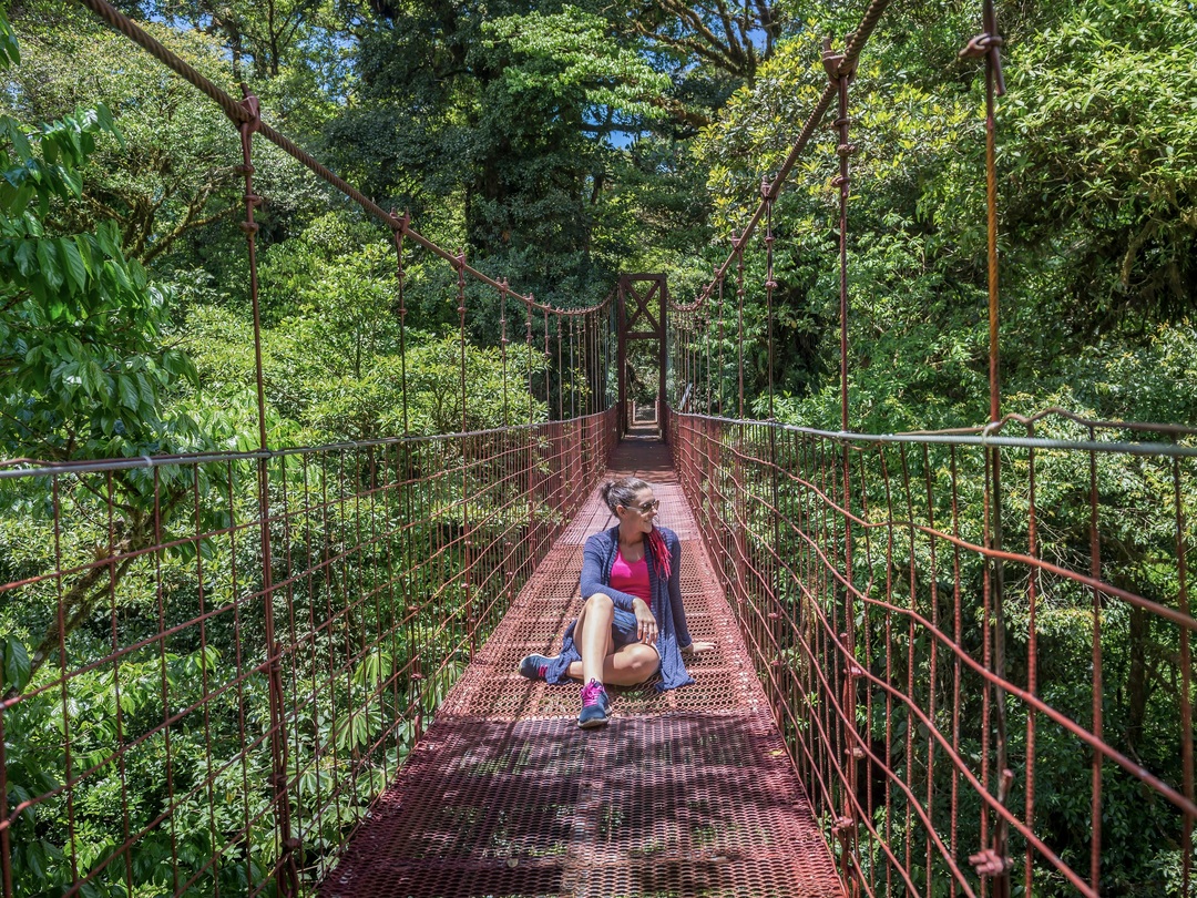 A lady sitting on a suspension bridge in Monteverde Toucan in the rainforest during the Other Way Round Travel group tour of Costa Rica